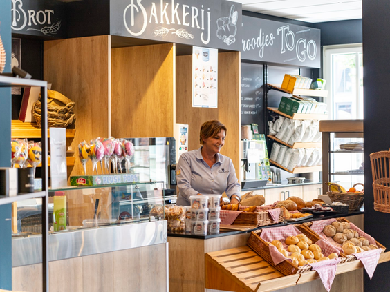 De parkwinkel en bakkerij op Dormio Resort Maastricht met een medewerker achter de toonbank vol verse broodjes en lekkernijen.