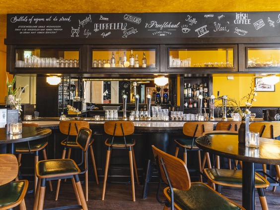 Het sfeervolle interieur van de bar in 't Proeflokaal, het grand café van Dormio Resort Maastricht, met hoge barkrukken.