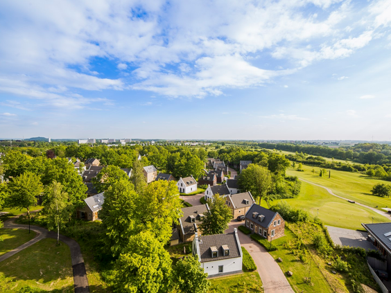 Luchtfoto van de luxe vakantiehuizen van Dormio Resort Maastricht, omgeven door bomen en groene velden.