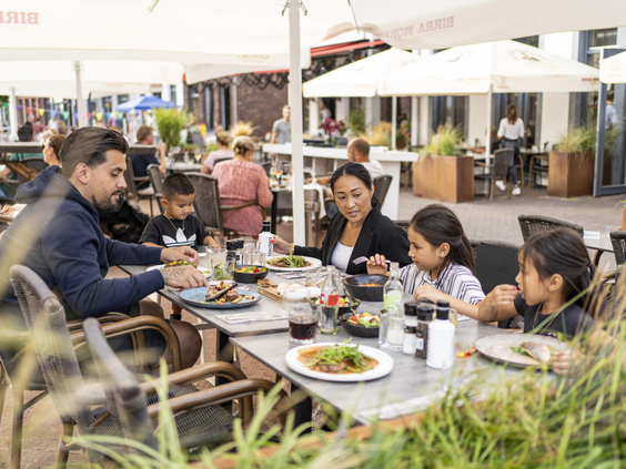 Een gezin geniet van een maaltijd op het gezellige, zonnige terras van een van de restaurants op Dormio Resort Maastricht.
