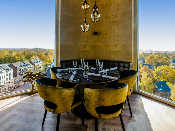 Een gedekte tafel in Rooftopbar De Dakkoffer met een spectaculair uitzicht over het Limburgse heuvelland en Dormio Resort Maastricht.