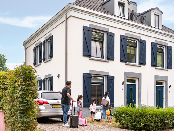 Een gezin met koffers arriveert bij hun luxe, witte vakantiewoning op Dormio Resort Maastricht voor hun vakantie.