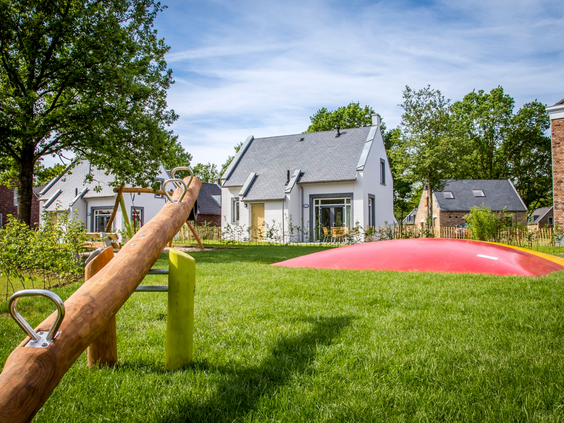Een speeltuin met een grote airtrampoline en een wipwap, gelegen op een grasveld direct voor de witte vakantiehuizen op Dormio Resort Maastricht.