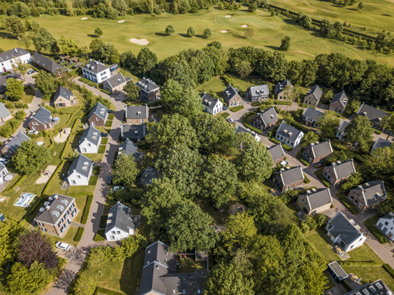 Luchtfoto van de luxe vakantiehuizen van Dormio Resort Maastricht, omgeven door bomen en groene velden.