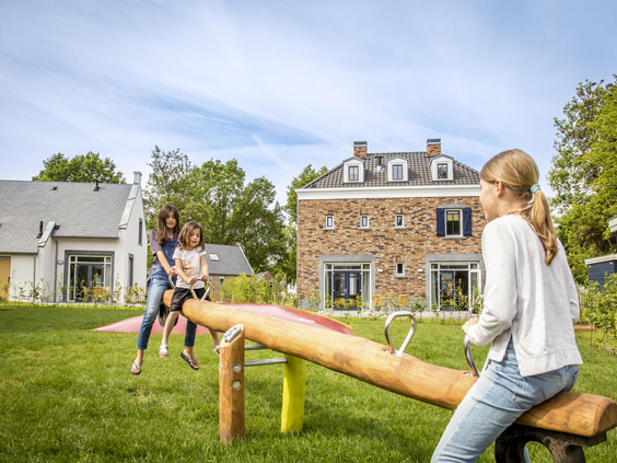 Kinderen en een moeder spelen samen op een grote houten wipwap in een van de speeltuinen op Dormio Resort Maastricht.