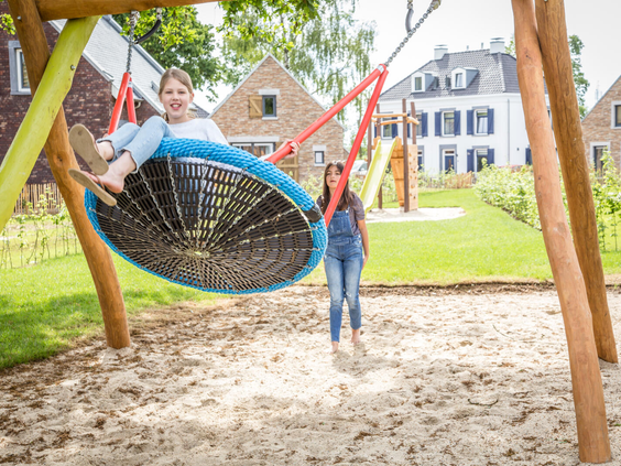 Twee meiden hebben plezier op de grote nestschommel in de zandspeeltuin van Dormio Resort Maastricht.