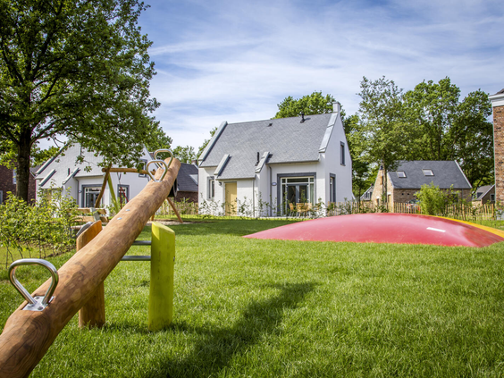 Een groot groen speelveld met een wipwap en een airtrampoline, gelegen tussen de moderne vakantiewoningen op Dormio Resort Maastricht.