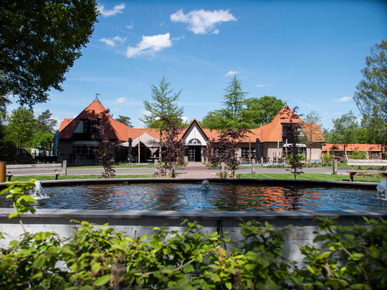 De entree van Resort Veluwe met een karakteristiek gebouw en een waterpartij, gelegen op de Veluwe.