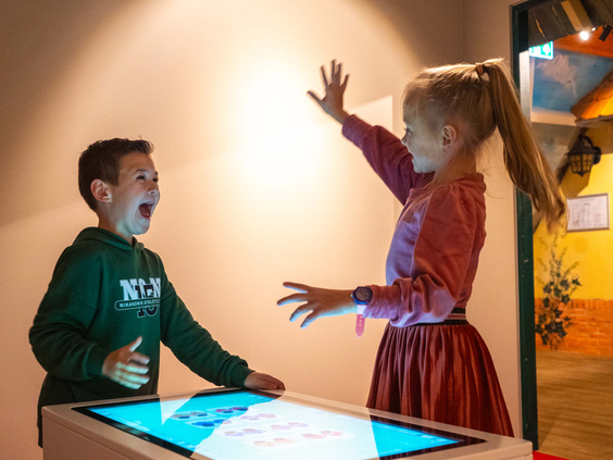 Kinderen spelen een interactief spel waarbij ze een muur aanraken op de Kimberley Kjaer speelzolder.