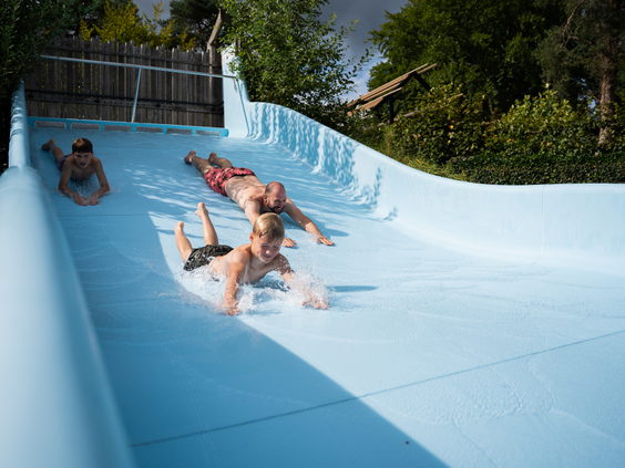 Kinderen glijden van de brede waterglijbaan het buitenzwembad in op Resort Veluwe.