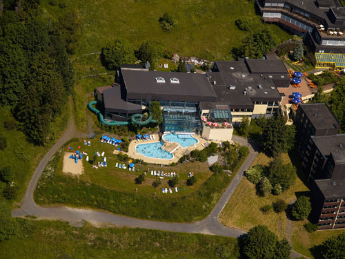 Luchtfoto van het Rhön Park Hotel in Beieren, met het buitenzwembad en de ligweide omgeven door de groene heuvels van de Rhön.