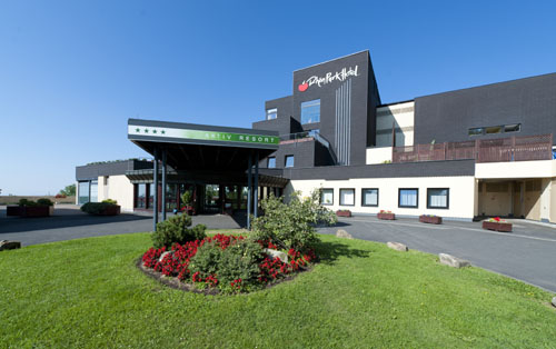 De moderne buitenkant en entree van het kindvriendelijke Rhön Park Hotel, omgeven door een verzorgde tuin met rode rozen.