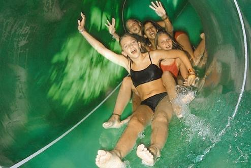 Een groep lachende meiden glijdt tegelijk van de brede, groene familieglijbaan in het zwemparadijs van het Rhön Park Hotel.