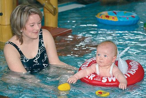 Een moeder geniet samen met haar baby, die in een veilige zwemring zit, van het warme water in het zwembad van het Rhön Park Hotel.