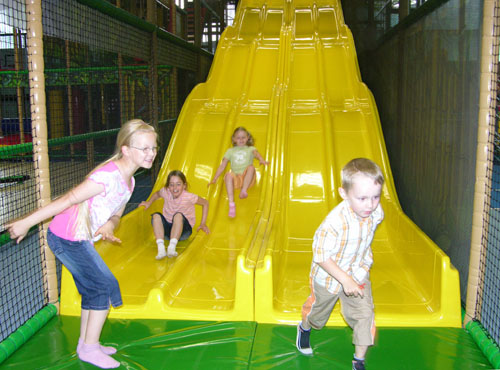 Kinderen glijden van brede gele glijbaan in indoorspeeltuin van Rhön Park Hotel Aktiv Resort in Beieren Duitsland