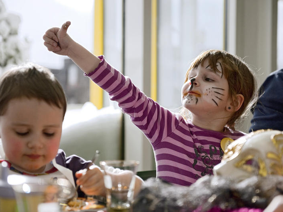 Een vrolijk meisje met haar gezicht geschminkt als een kat doet mee met de kinderanimatie in het Rhön Park Hotel.
