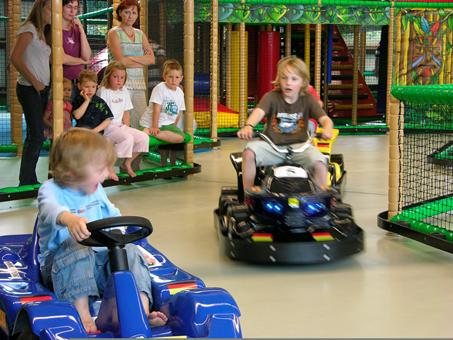 Kinderen racen vol plezier op de indoor kartbaan met elektrische skelters in de binnenspeeltuin van het Rhön Park Hotel.
