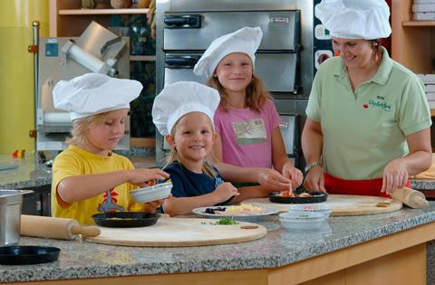 Kinderen met koksmutsen op zijn druk bezig met het beleggen van hun eigen mini-pizza's tijdens een kookworkshop in het Rhön Park Hotel.