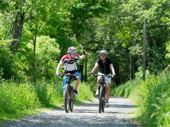 Twee kinderen of tieners fietsen op mountainbikes over een pad door het bos in de heuvelachtige omgeving van Rhön Park Aktiv Resort.