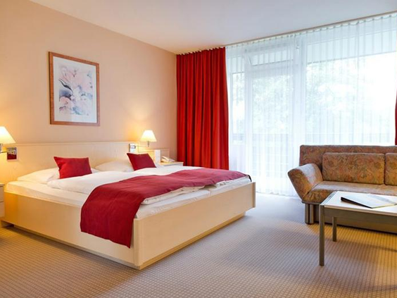 De nette slaapkamer van een hotelkamer of appartement in Rhön Park Aktiv Resort, met een opgemaakt tweepersoonsbed en rode accenten.