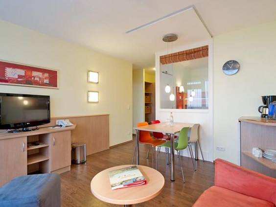 De woonkamer en het eetgedeelte van een appartement in Rhön Park Aktiv Resort, met een zithoek, televisie en eettafel.