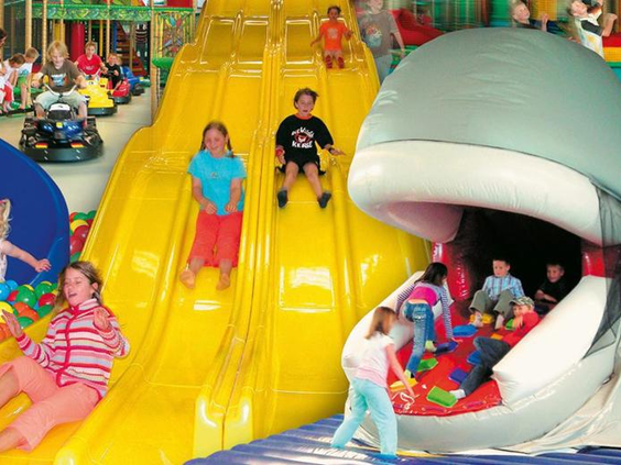 Kinderen glijden lachend van de grote gele glijbaan in de ballenbak van indoorspeeltuin Rudis Abenteuerland bij Rhön Park Aktiv Resort.