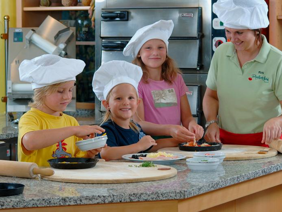 Lachende kinderen met koksmutsen op zijn bezig met een workshop pizza bakken bij Rhön Park Aktiv Resort.