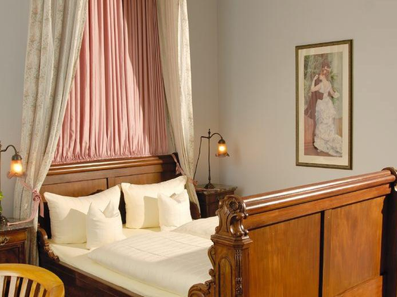 Detail van een klassiek en sierlijk houten bed met een roze baldakijn in een van de kamers van Hotel Bellevue.