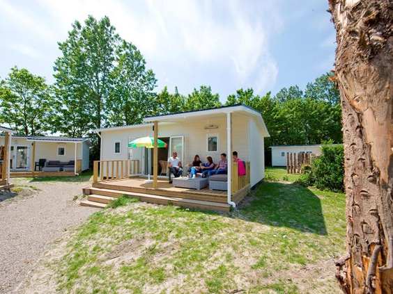 Een gezellige stacaravan met een overdekte houten veranda en een familie die buiten zit op Roompot Beach Resort.