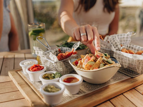 Een houten borrelplank met een schaal nacho's, diverse hapjes en verschillende dipsauzen die gedeeld wordt op een terras.
