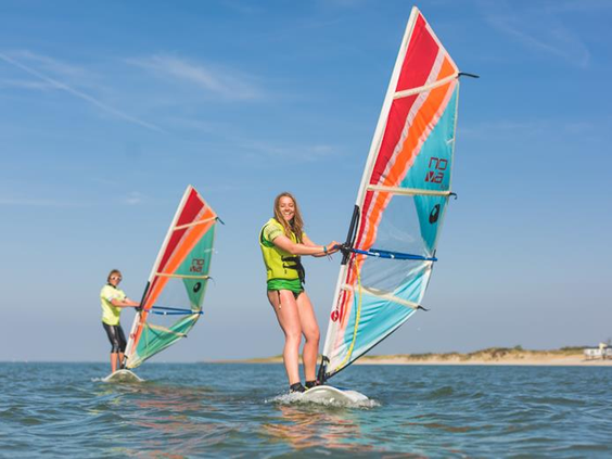 Twee mensen zijn aan het windsurfen op het kalme water van de Oosterschelde op een zonnige dag bij Roompot Beach Resort.