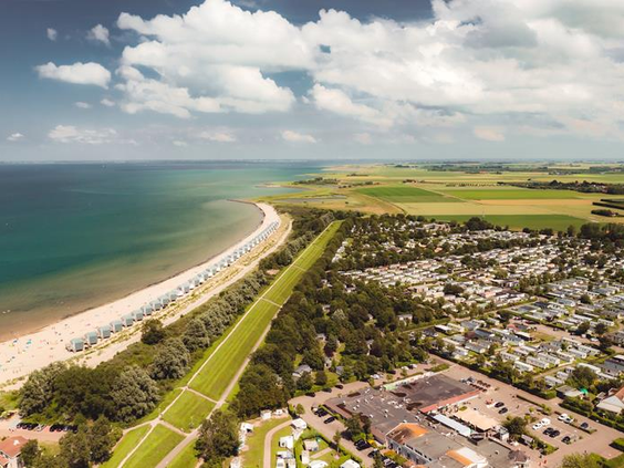 Luchtfoto van het brede zandstrand en de vakantiehuisjes van Roompot Beach Resort aan de Zeeuwse kust.