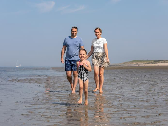 Een gezin met een jong kind wandelt en zoekt schelpen op het strand bij laagwater aan de Oosterschelde.