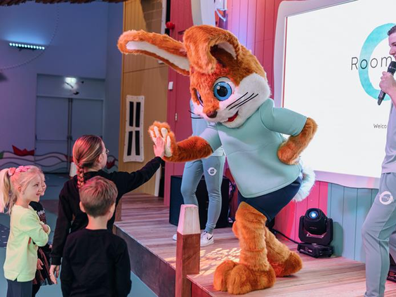 Kinderen geven een high five aan mascotte Koos Konijn die op het podium staat tijdens een show in de Koos Kids Club.