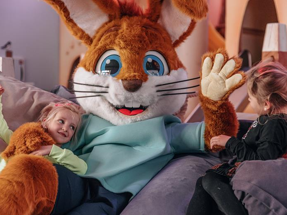 Twee blije kinderen geven een dikke knuffel aan de grote, zachte mascotte Koos Konijn van Roompot.