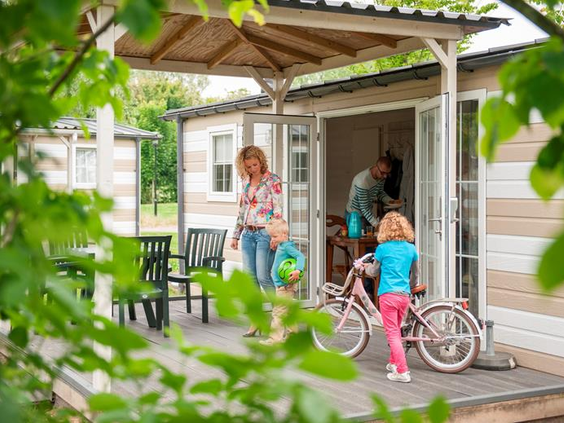 Een gezin met kinderen staat bij de openslaande deuren van hun chalet met veranda op Roompot Beach Resort.