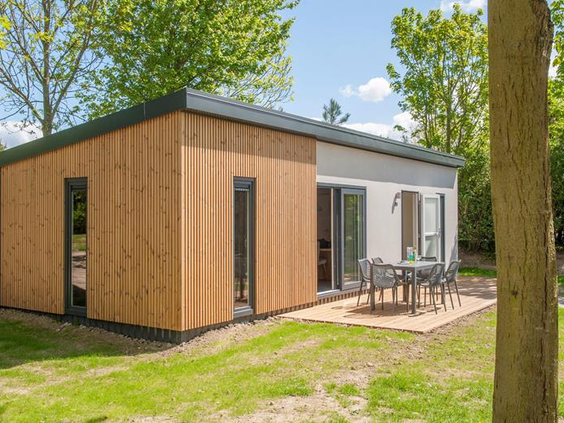 De buitenkant van een moderne en luxe lodge met houten gevel en een ruim terras op Roompot Beach Resort.