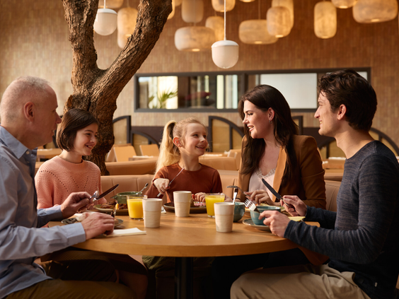Gezin met drie generaties geniet samen van ontbijt aan ronde houten tafel in restaurant van Safari Hotel Beekse Bergen