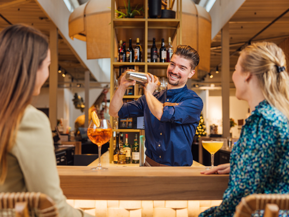 Een lachende bartender schudt een cocktail voor twee gasten aan de bar van Safari Hotel Beekse Bergen