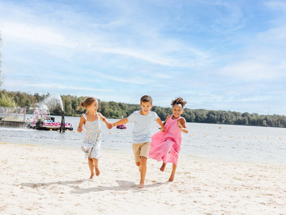 Drie vrolijke kinderen rennen hand in hand over het zandstrand van Beekse Bergen