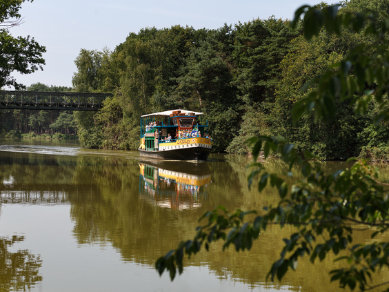 De safariboot vaart met bezoekers over het water langs de groene oevers van Beekse Bergen