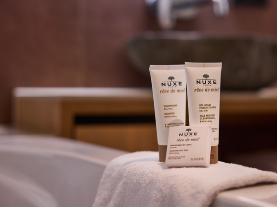 Luxe badproducten van het merk Nuxe op de rand van het bad in een hotelkamer van het Safari Hotel.