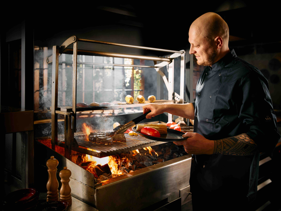 Chef‑kok bereidt gegrilde groenten en vlees op grote open houtskoolgrill tijdens live cooking diner in restaurant van Safari Resort Beekse Bergen