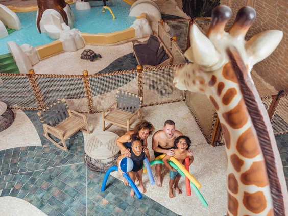 Gezin speelt met zwemschuimen in het binnenzwembad met safarithema en grote giraffebeeld bij Safari Resort Beekse Bergen