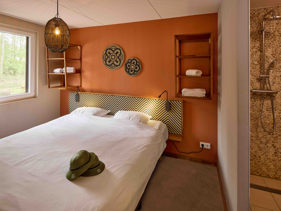 safari-thema tweepersoons slaapkamer in Safari Resort Beekse Bergen met opgemaakt bed en een moderne badkamer met inloopdouche