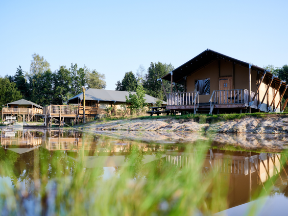De houten safaritenten van Vakantiepark Sallandshoeve weerspiegelen prachtig in het kalme water van de natuurlijke speelvijver.