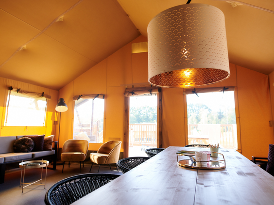 Het sfeervolle en ruime interieur van een safaritent op Sallandshoeve, met een lange eettafel en een comfortabele zithoek.
