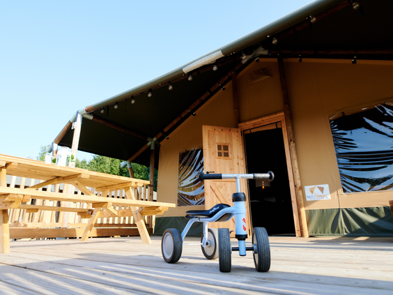Een stoere blauwe driewieler staat klaar op de ruime houten veranda van een safaritent op Vakantiepark Sallandshoeve.