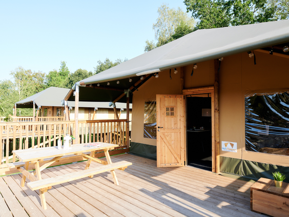 De grote, zonnige houten veranda van een safaritent, compleet met een robuuste picknicktafel, op Vakantiepark Sallandshoeve.