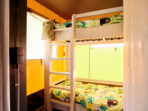 De gezellige kinderslaapkamer in een safaritent, met een houten stapelbed en vrolijk beddengoed, op Vakantiepark Sallandshoeve.